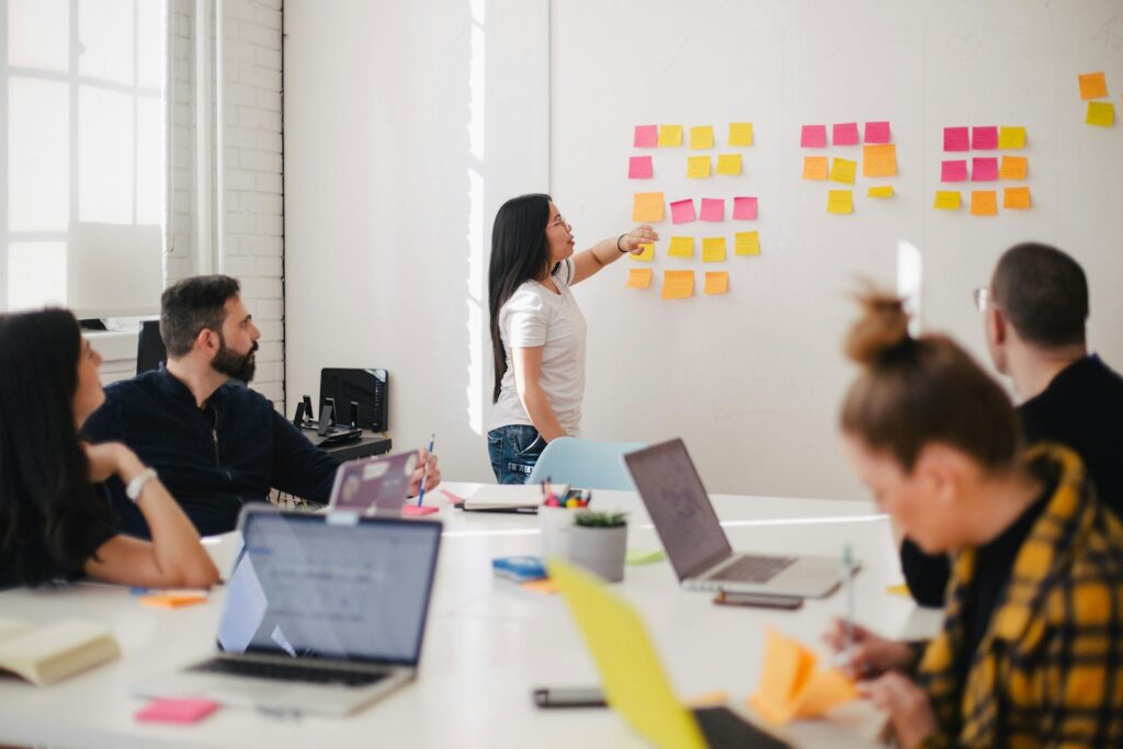 Femme plaçant des post-its sur un mur et en discutant avec d'autres personnes.